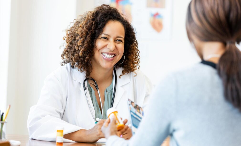 Happy Sol Health medication management telehealth visit with a clinician in a white coat, smiling and wearing a stethoscope in a bright room